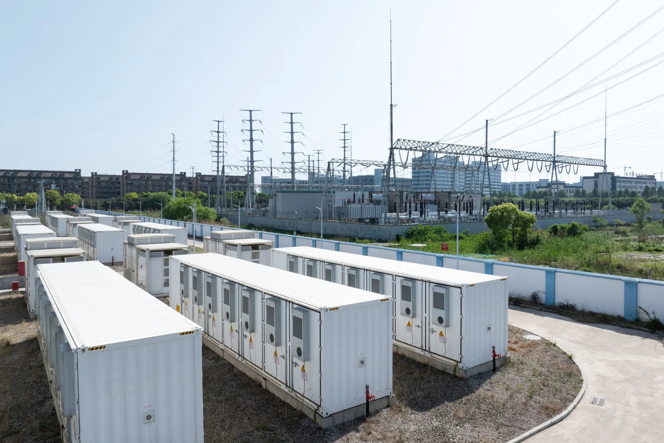 A grid-scale battery storage field of white containers beside an electrical substation